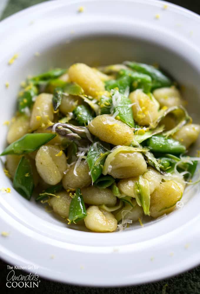 A close up overhead photo of pan seared gnocchi with shaved asparagus and snap peas in a white bowl.