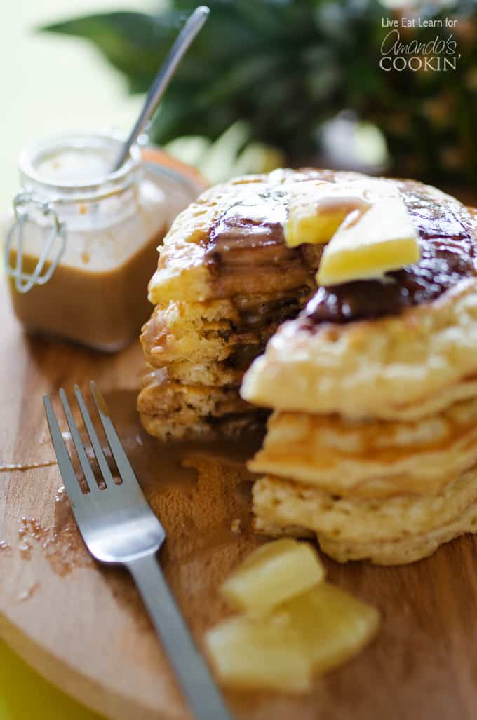 A close up photo of a stack of pineapple pancakes cut into on a wooden cutting board.