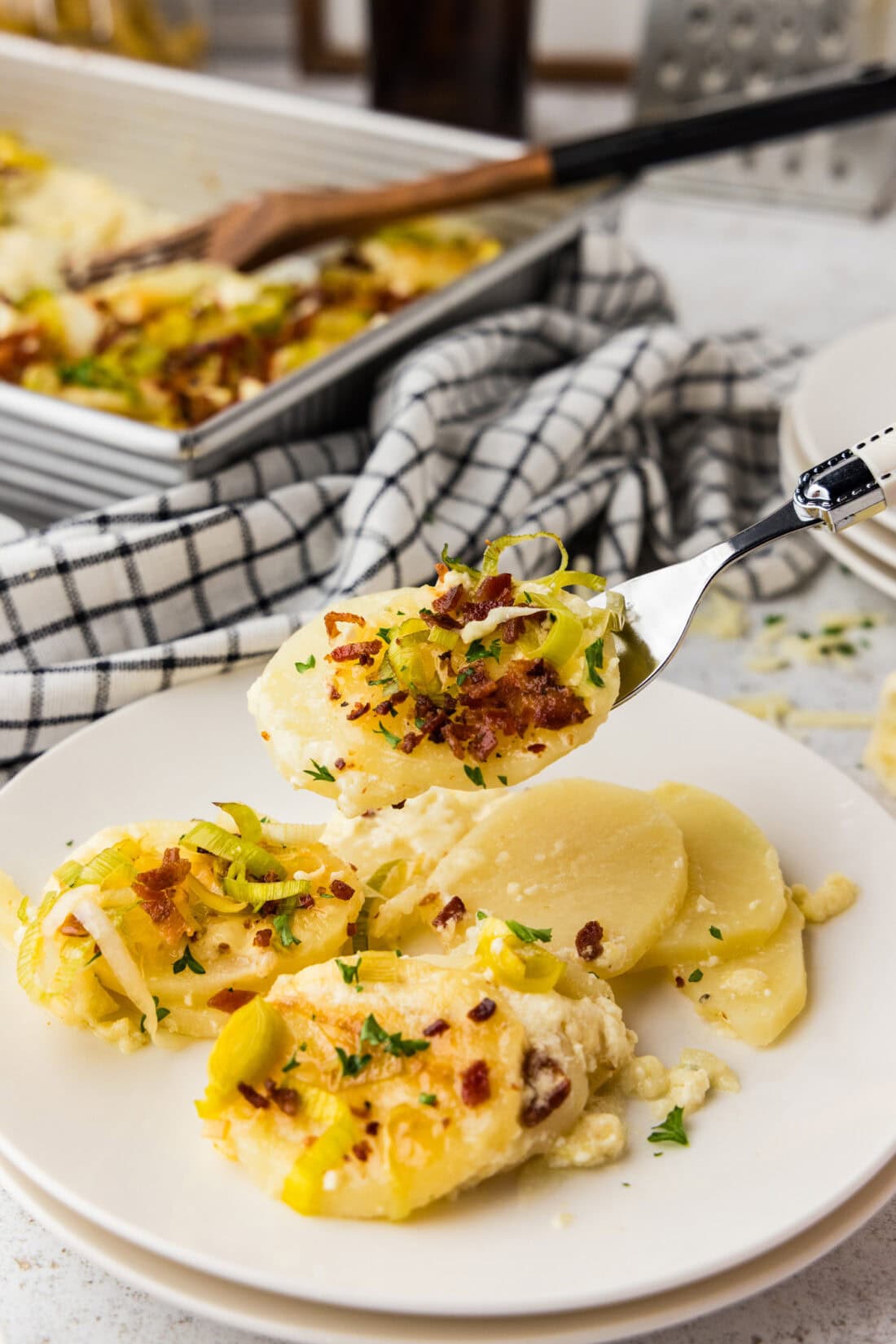 A close up of a forkful of potatoes au gratin with bacon and leeks.