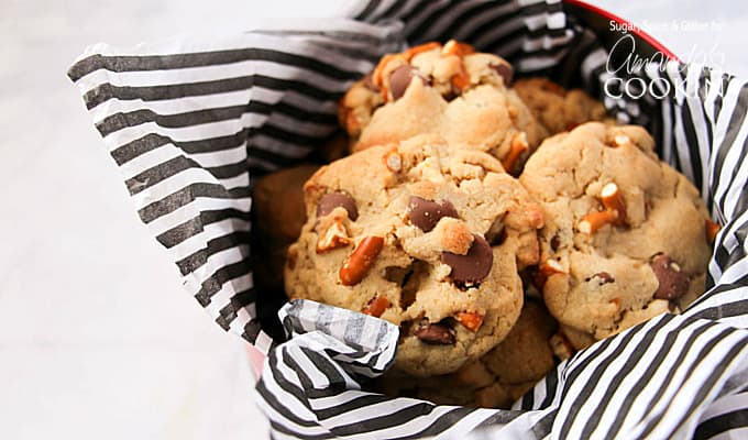 A close up photo of pretzel chocolate chip cookies in a tin lined with black and white striped tissue paper.
