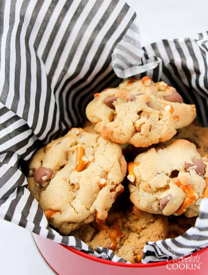 A photo of pretzel chocolate chip cookies in a tin lined with black and white striped tissue paper.