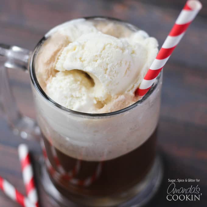 A photo of a root beer float cocktail in a clear mug served with a red and white striped straw.