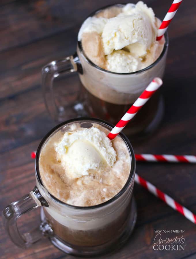 An overhead photo of two root beer float cocktails in clear mugs served with a red and white striped straw.