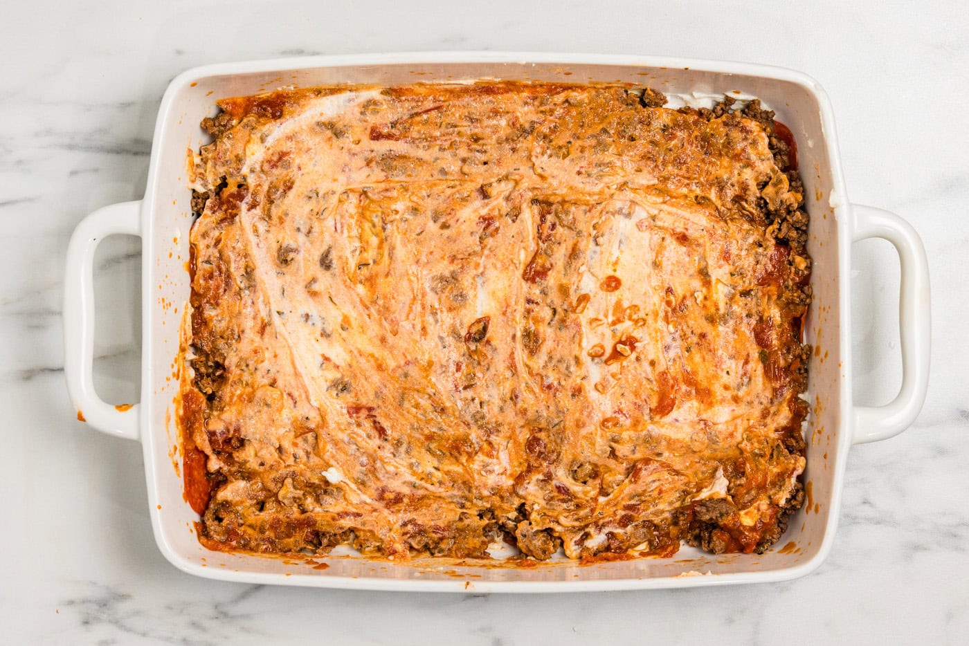 ricotta cheese spread over meat sauce in baking dish