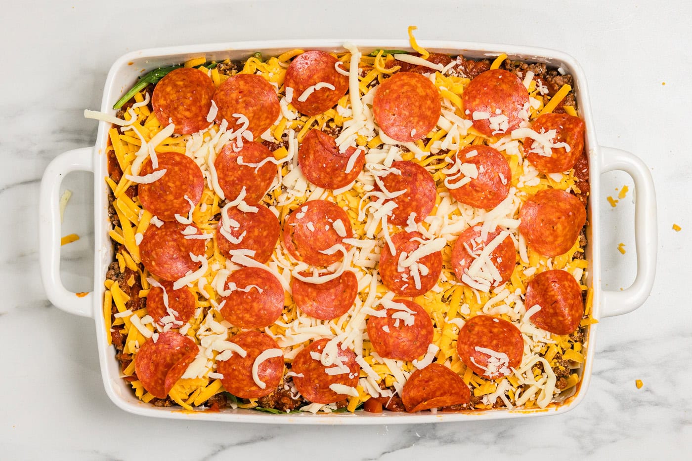 pepperoni slices over shredded cheese in baking dish