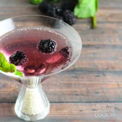 A close up of a blackberry gin martini topped with fresh blackberries and mint leaves.