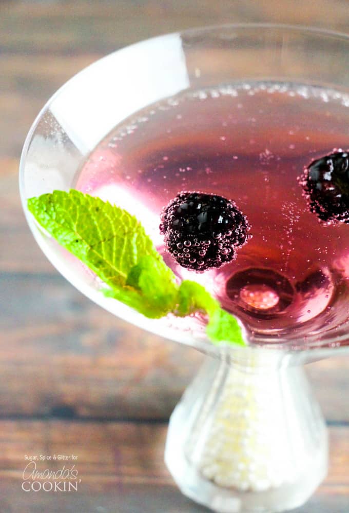 A close up overhead of a blackberry gin martini topped with fresh blackberries and mint leaves.