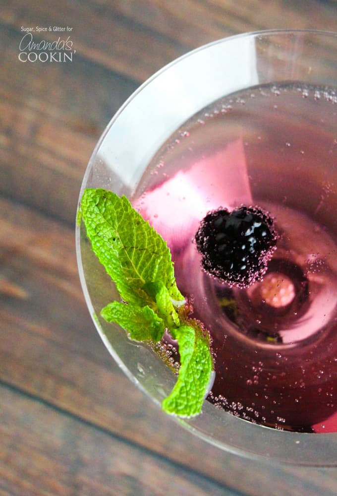 A close up overhead of a blackberry gin martini topped with fresh blackberries and mint leaves.