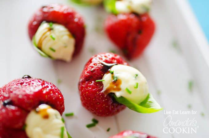 A close up photo of strawberries stuffed with whipped brie and topped with a basil leaf.