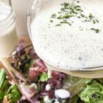 A close up photo of buttermilk ranch dressing being poured over a salad.