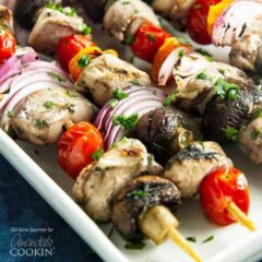 A close up of marinated chicken skewers  with tomatoes, red onions and mushrooms.