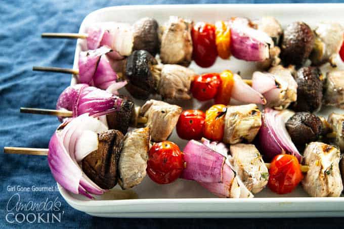 A close up of marinated chicken skewers  with tomatoes, red onions and mushrooms.