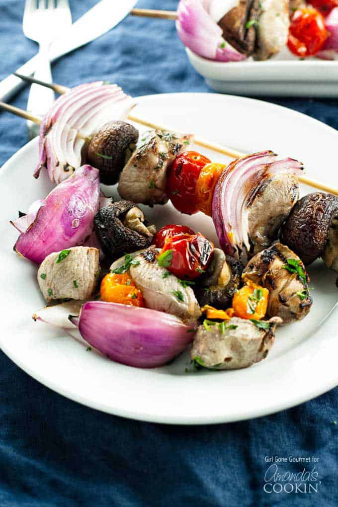 A close up photo of marinated grilled chicken skewers on a white plate.