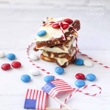 Patriotic candy bark stacked on top of each other with American flags and red, white and blue M&Ms scatted in the background.
