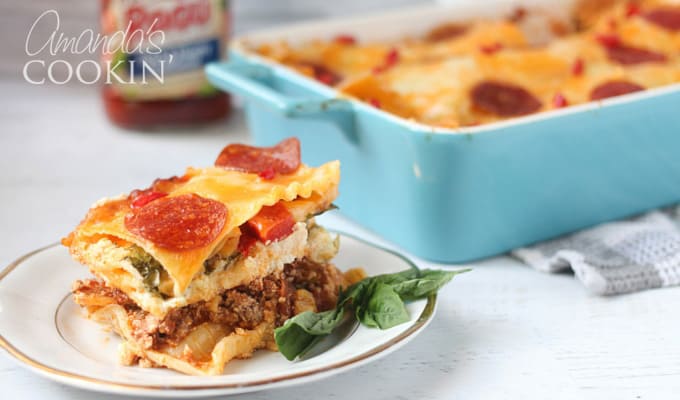 A close up of pizza lasagna on a white and gold plate with the full dish in the background.