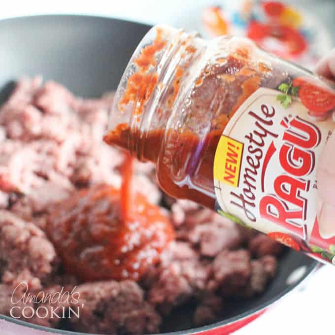 A close up photo of Ragu sauce being poured into a skillet of ground beef.