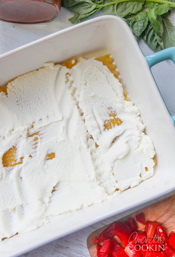 An overhead photo of lasagna noodles in a pan with ricotta cheese spread on top.