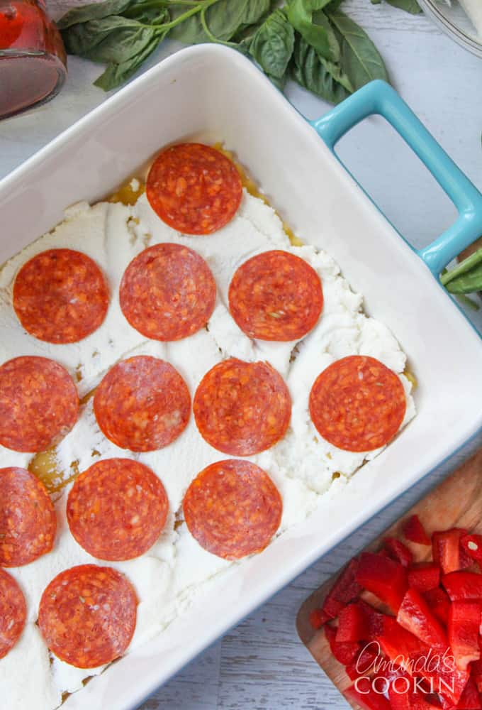 An overhead photo of lasagna noodles in a pan with ricotta cheese spread on top and pepperoni. 