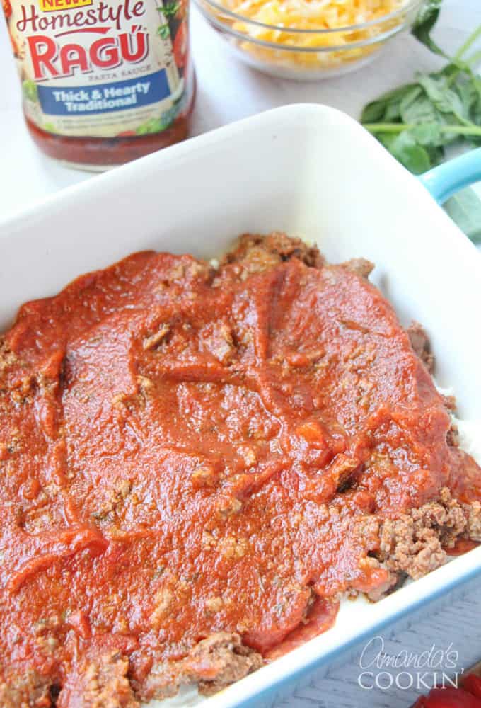 An overhead photo of homestyle Ragu sauce poured over ground beef, pepperoni, ricotta cheese and lasagna noodles in a dish.