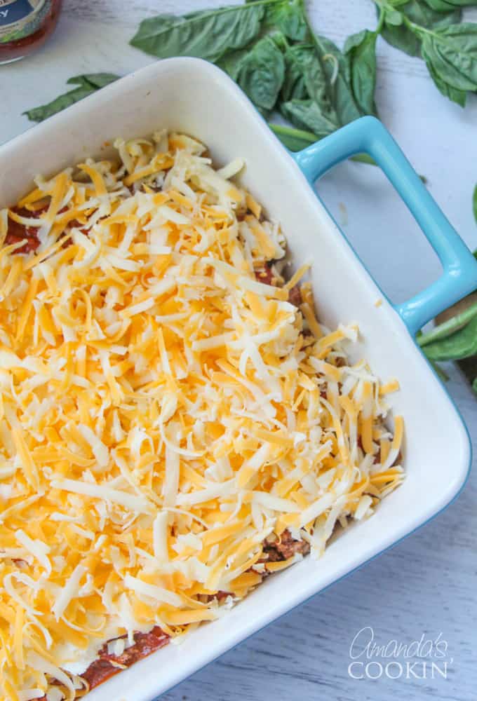 An overhead photo of shredded cheese over homestyle Ragu sauce, ground beef, pepperoni, ricotta cheese and lasagna noodles in a dish.