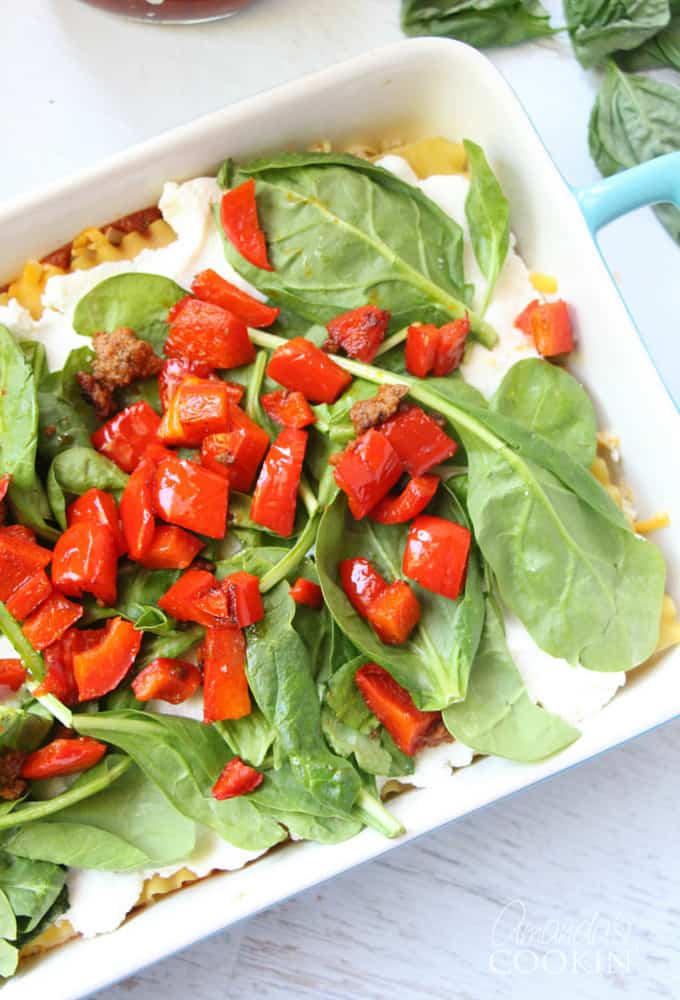 A photo of ricotta cheese on the lasagna noodles, spinach over that and chopped peppers on top.