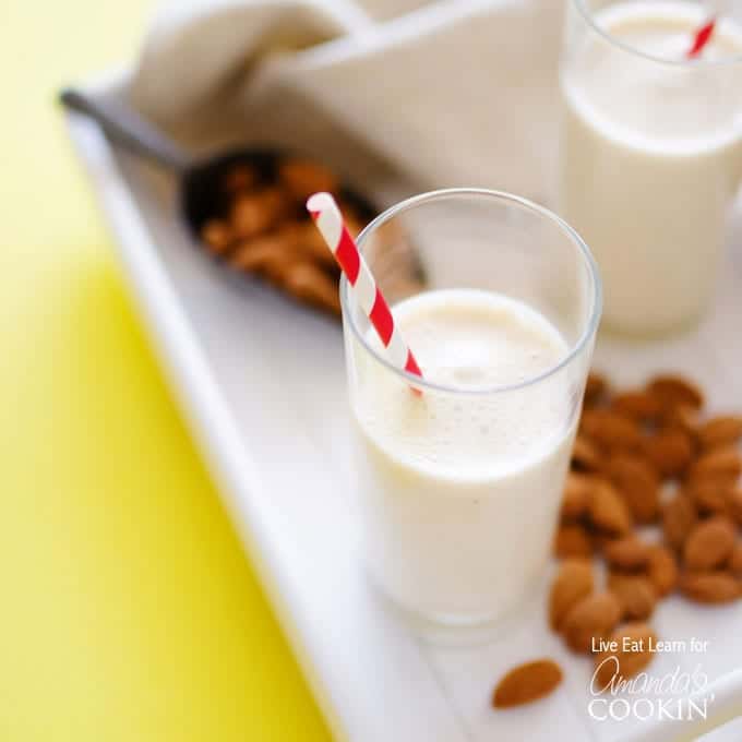 An overhead of a tall clear glass filled with an almond maple smoothie and served with a red and white straw.