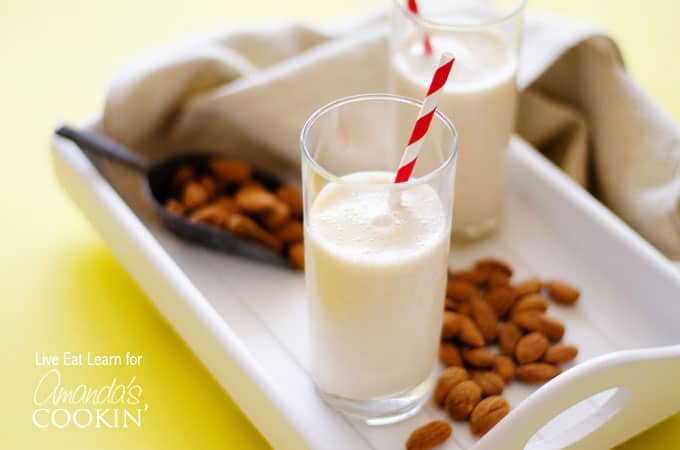 An almond maple smoothie resting on a white plate with scattered almonds.