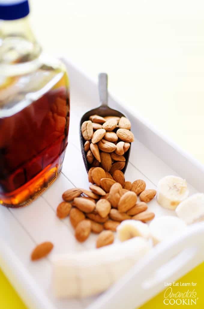 A close up photo of a jar of maple syrup and a scoop of almonds.