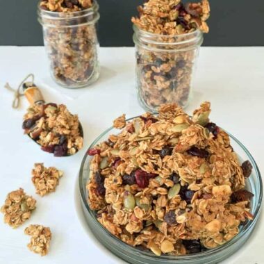 A photo of a plate of autumn harvest fruit and nut granola and two filled mason jars in the background.