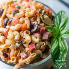 A close up of a bowl filled with Mediterranean pasta salad and a basil leaf on the side.