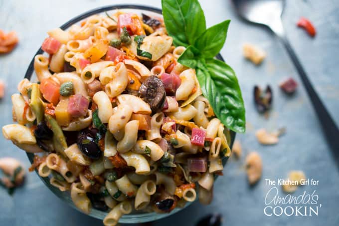 A close up of a bowl filled with Mediterranean pasta salad and a basil leaf on the side.