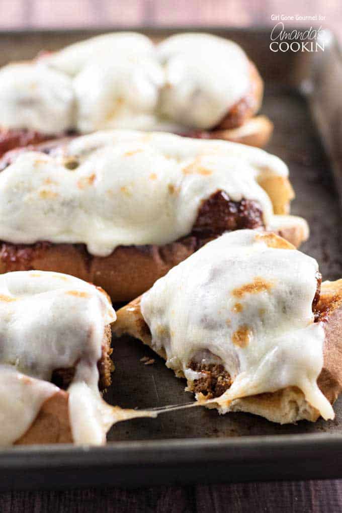 A close up photo of a slow cooker BBQ meatball sub topped with provolone cheese cut in half with two others in the background. 