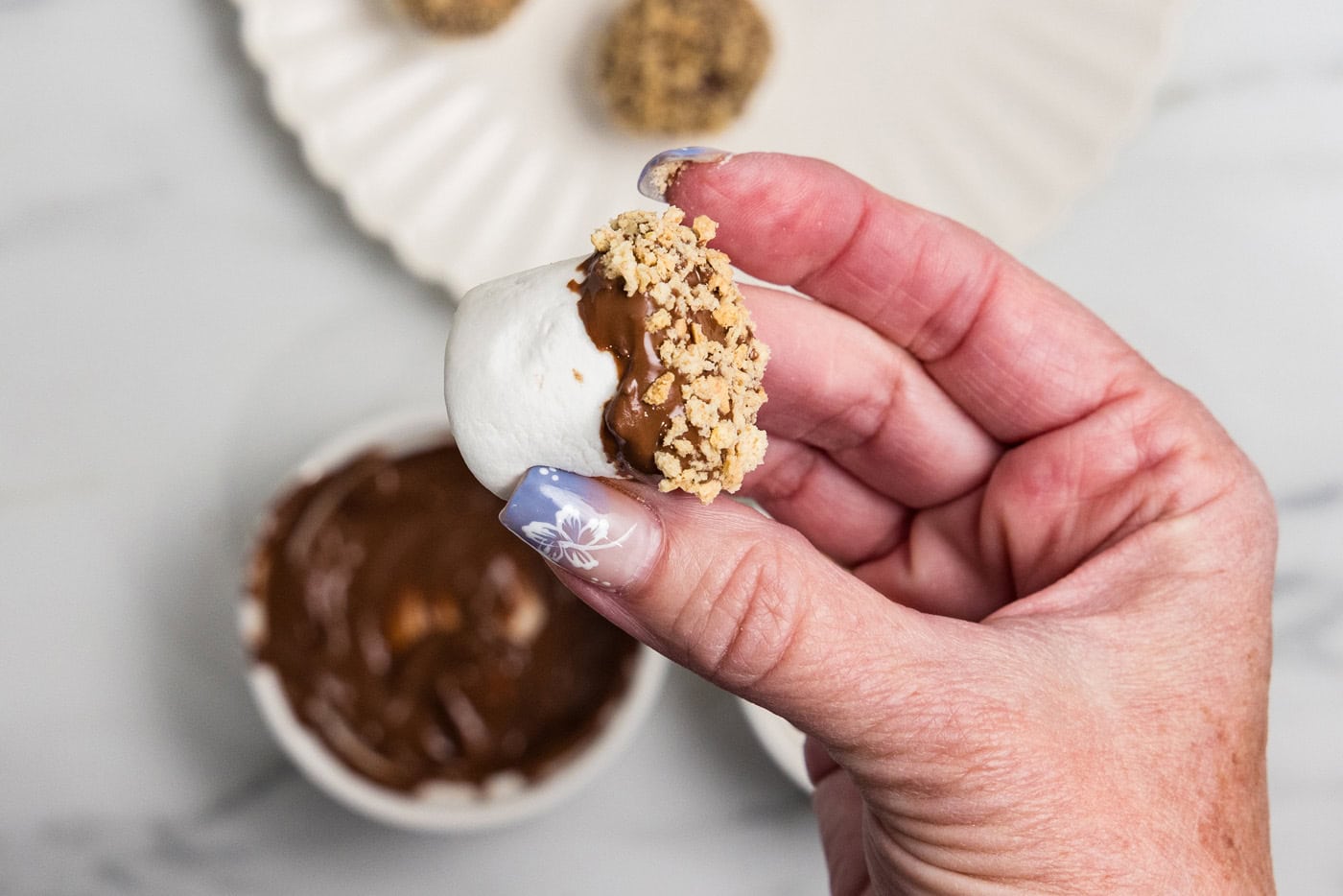 holding a marshmallow with melted chocolate and graham cracker crumbs