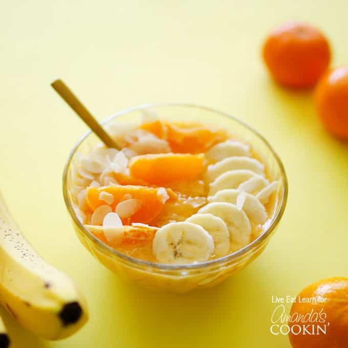 A close up of an almond orange smoothie bowl topped with mandarine oranges and sliced banana.