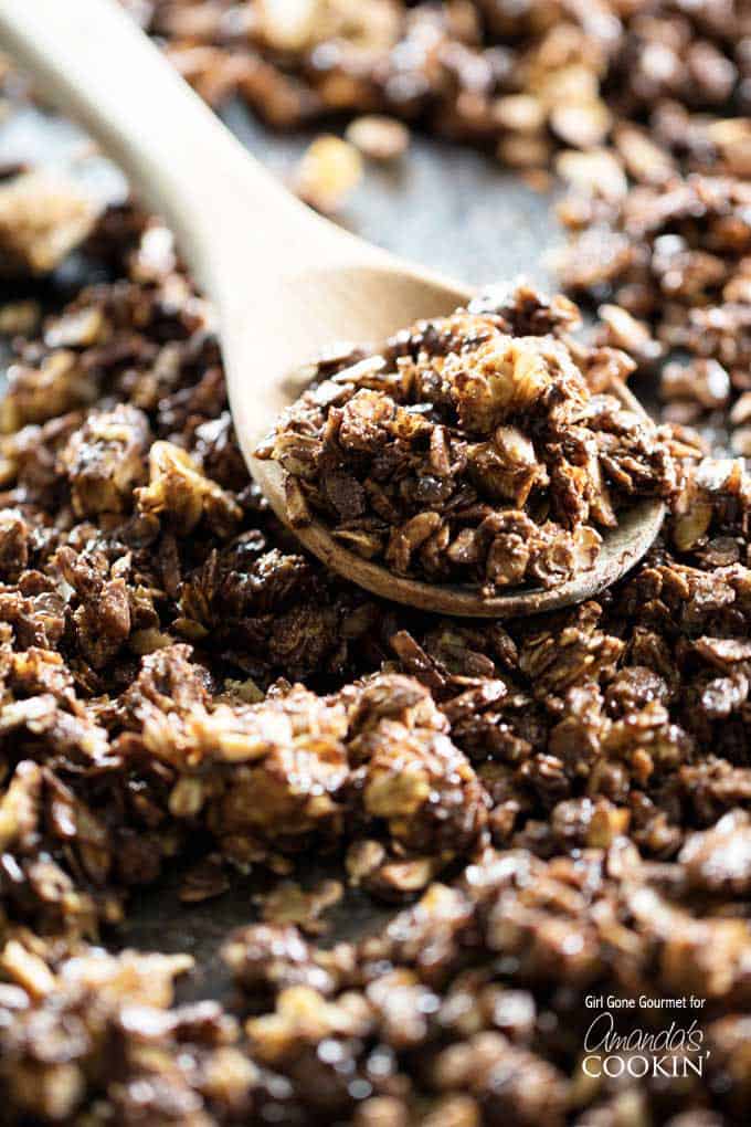 A close up photo of homemade dark chocolate granola scooped into a wooden spoon.