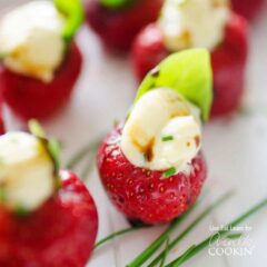 A close up photo of strawberries filled with whipped brie and topped with a basil leaf.