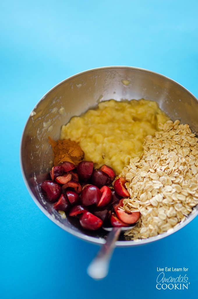 A stainless steel bowl filled with mashed bananas, chopped cherries and rolled oats.