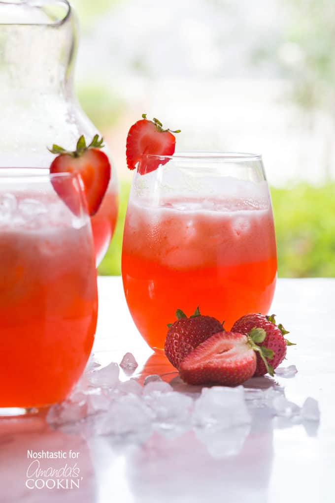 Two short glasses filled with strawberry lemonade served with sliced strawberries on the rim of the glass and on the side.
