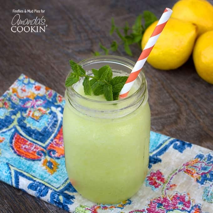 A mason jar filled with honeydew lemon slush topped with fresh mint and served with a red and white striped straw.