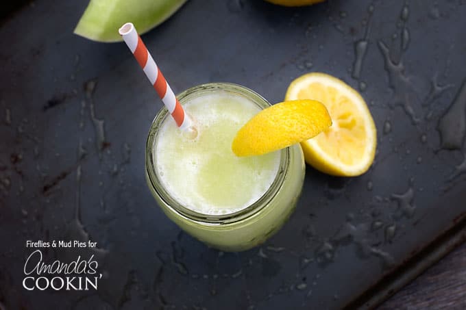 A overhead of a mason jar filled with honeydew lemon slush topped with a lemon wedge and served with a red and white striped straw.