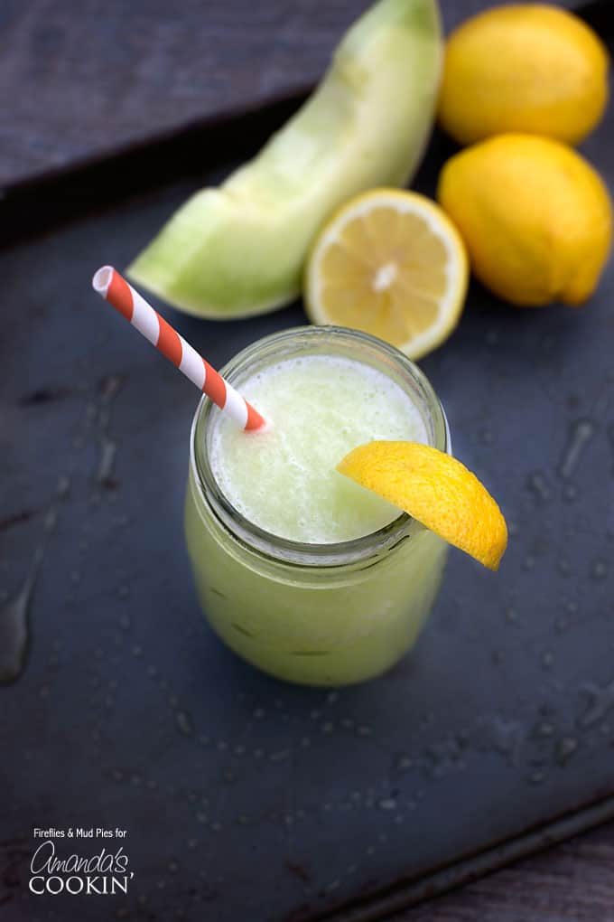 A overhead of a mason jar filled with honeydew lemon slush topped with a lemon wedge and served with a red and white striped swear.
