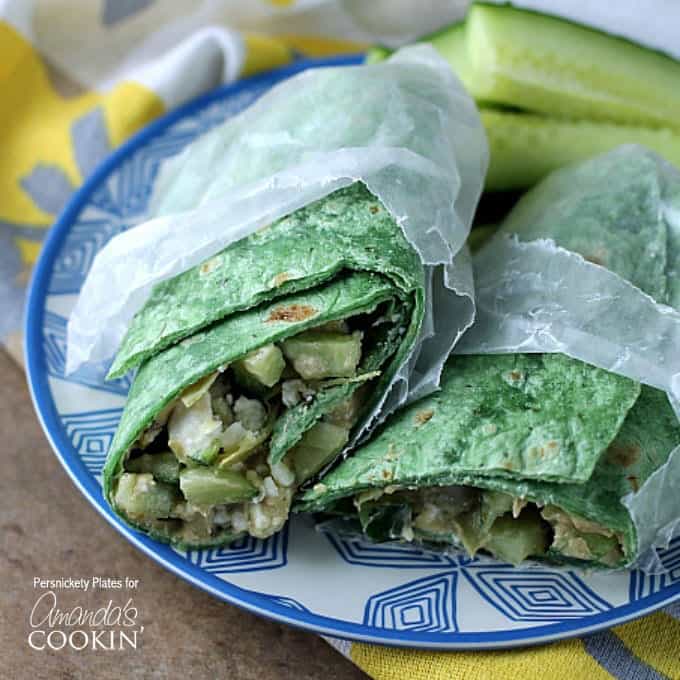 Two halves of a Mediterranean veggie wrap in wax paper resting next to each other on a blue and white plate.