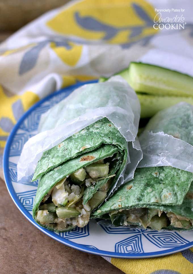 Two halves of a Mediterranean veggie wrap in wax paper resting next to each other on a blue and white plate.