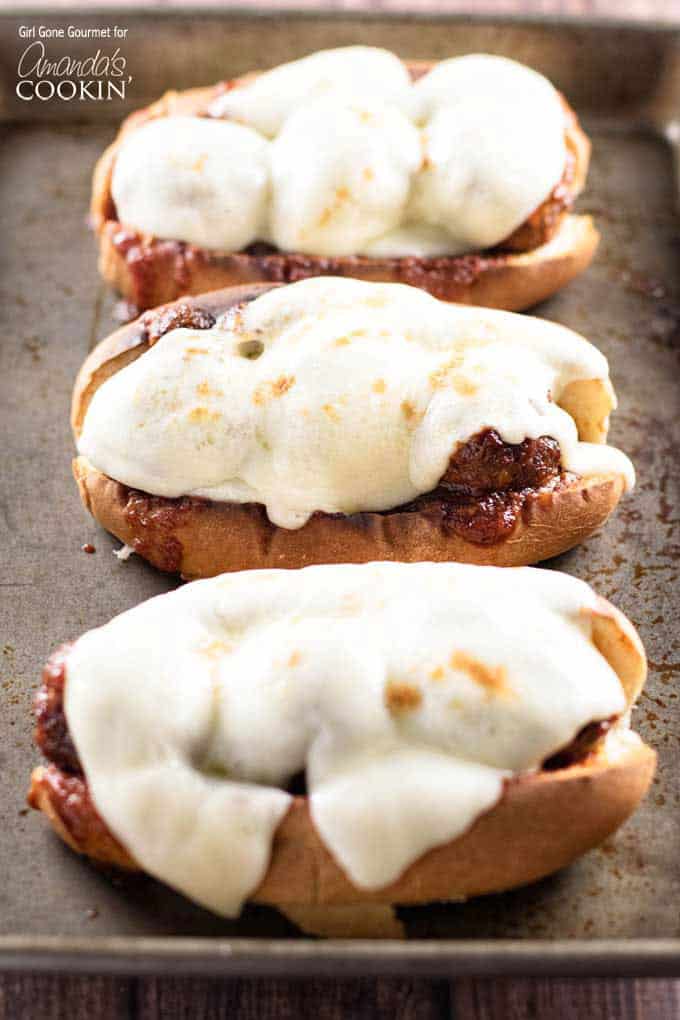 A close up photo of three slow cooker BBQ meatball subs topped with provolone cheese.