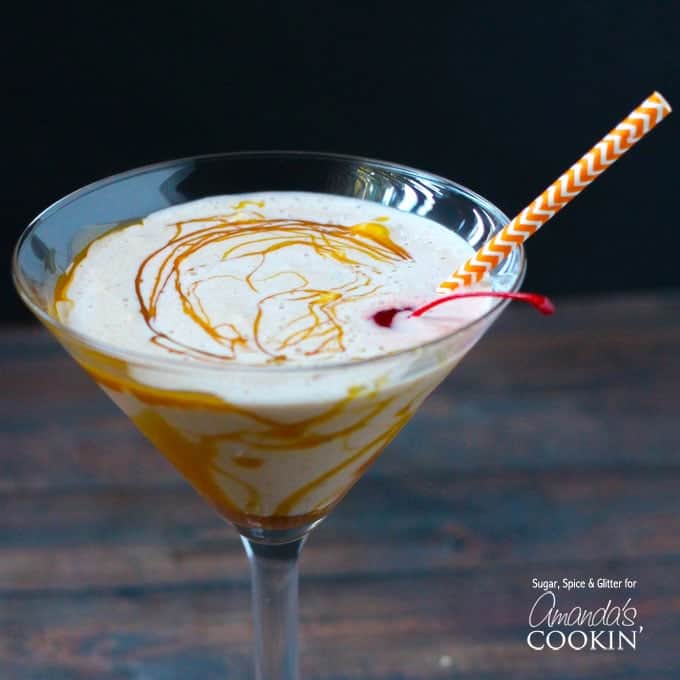 A close up of a clear martini glass filled with a butterscotch milkshake cocktail topped with a cherry and a straw.