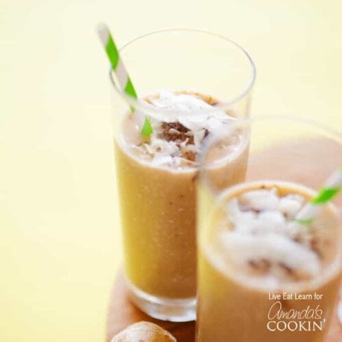 Two tall clear glasses filled with a cozy coconut smoothie and served with a green and white striped straw.