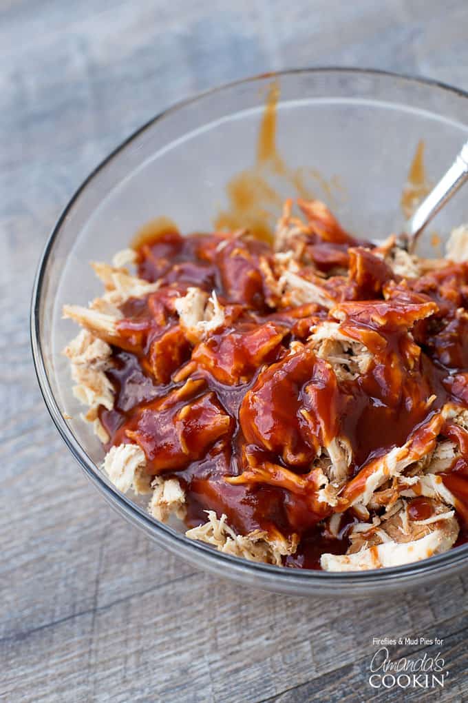 A clear bowl of shredded chicken with BBQ sauce on top.