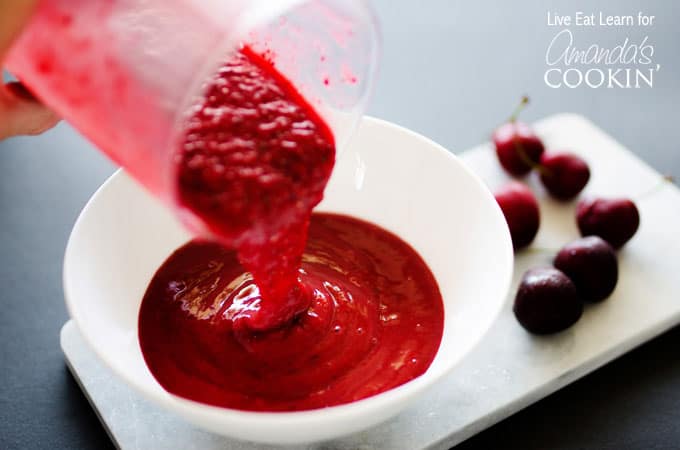 A close up photo of stone fruit smoothie being poured into a bowl.