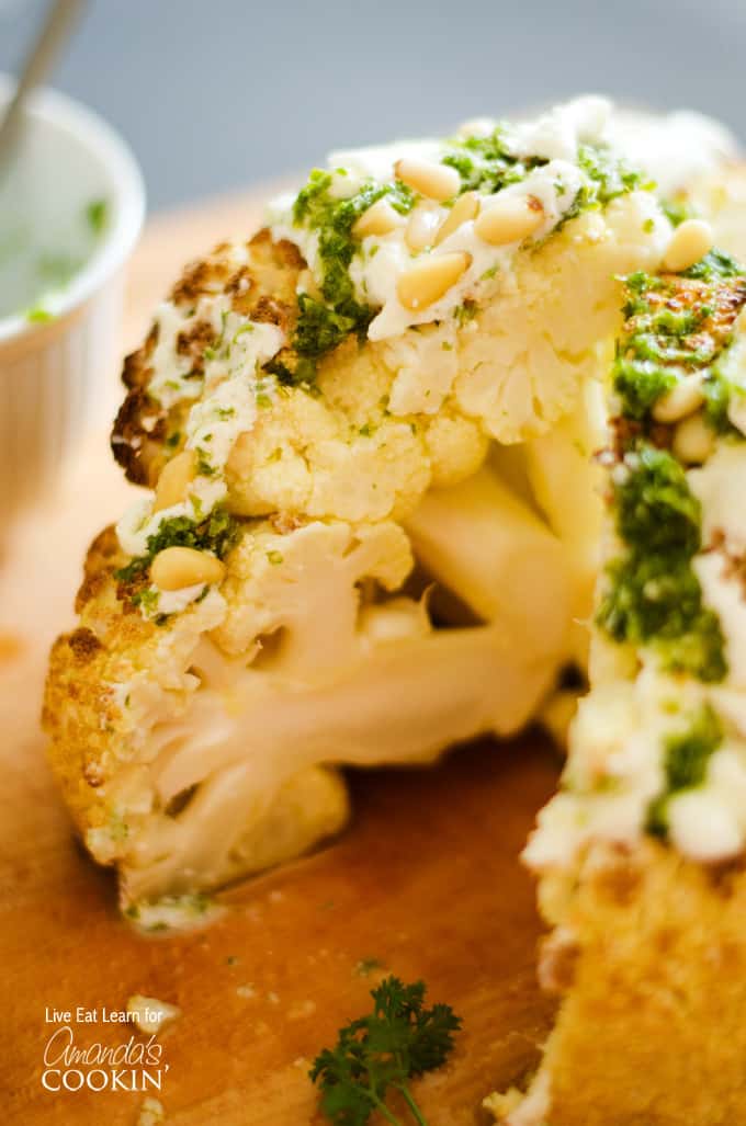 A close up of the center of a whole roasted cauliflower topped with whipped feta and herb sauce on a wooden cutting board.