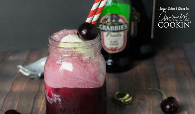 A close up of a mason jar filled with a black cherry float cocktail and served with red and white straws and topped with a cherry.